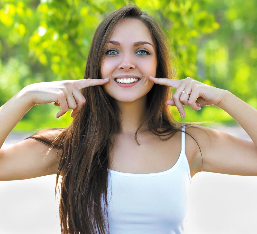 mujer con dientes blancos sonriendo y señalando su rostro