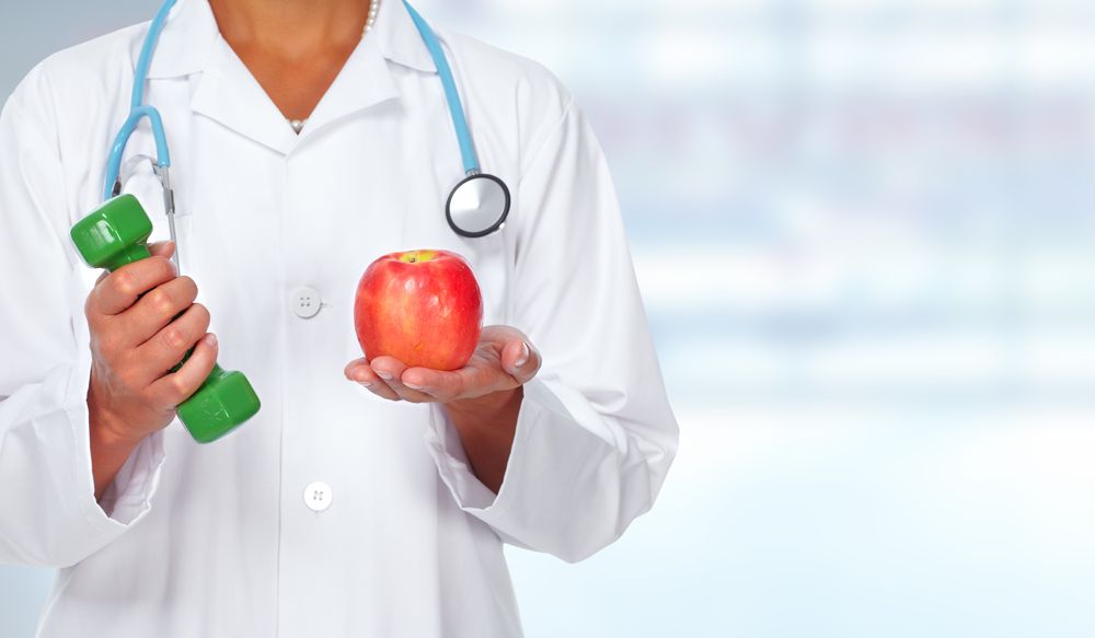 médico con estetoscopio en el cuello, una mancuerna y manzana en las manos