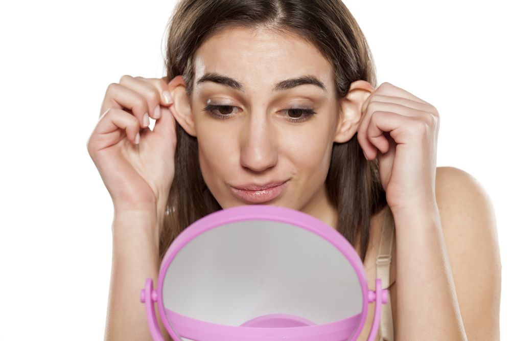 mujer estirando sus orejas frente a un espejo
