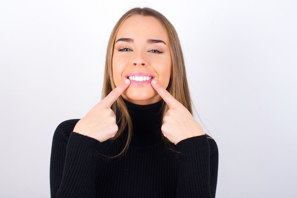 Mujer señalando sus dientes blancos