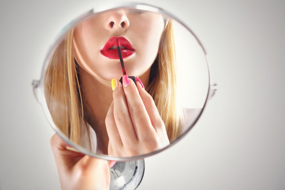 mujer pintando sus labios frente a un espejo